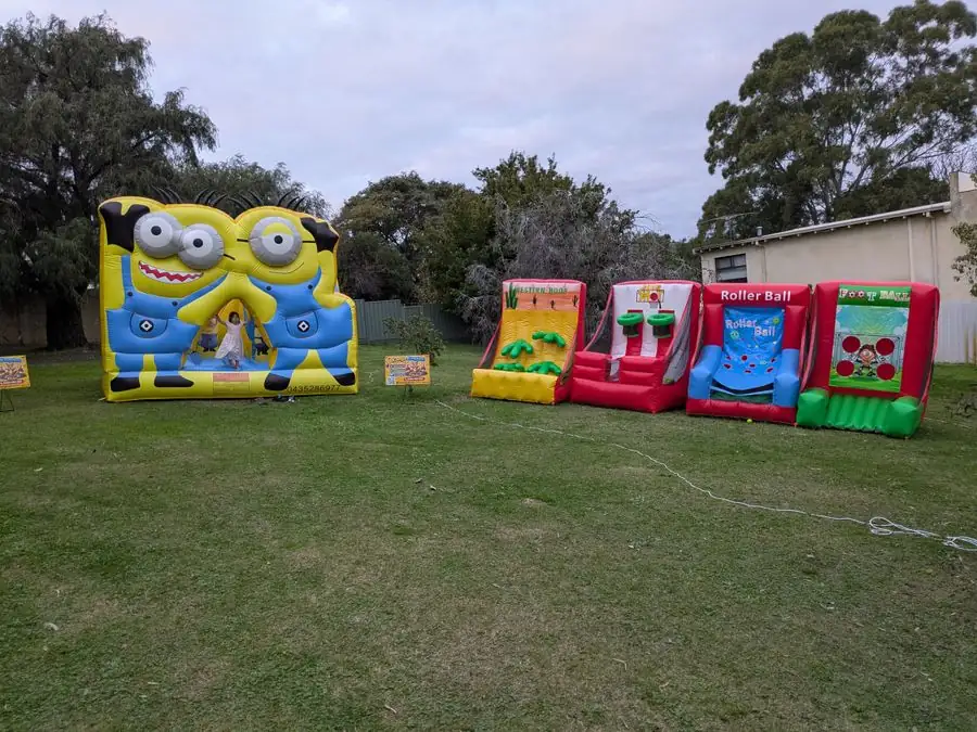 Minions bouncy castle and four inflatable carnival games set up together on a grassy reserve
